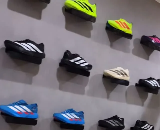A parede cinza da loja cheia de Adizero e Alphafly, um par em cada prateleira preta