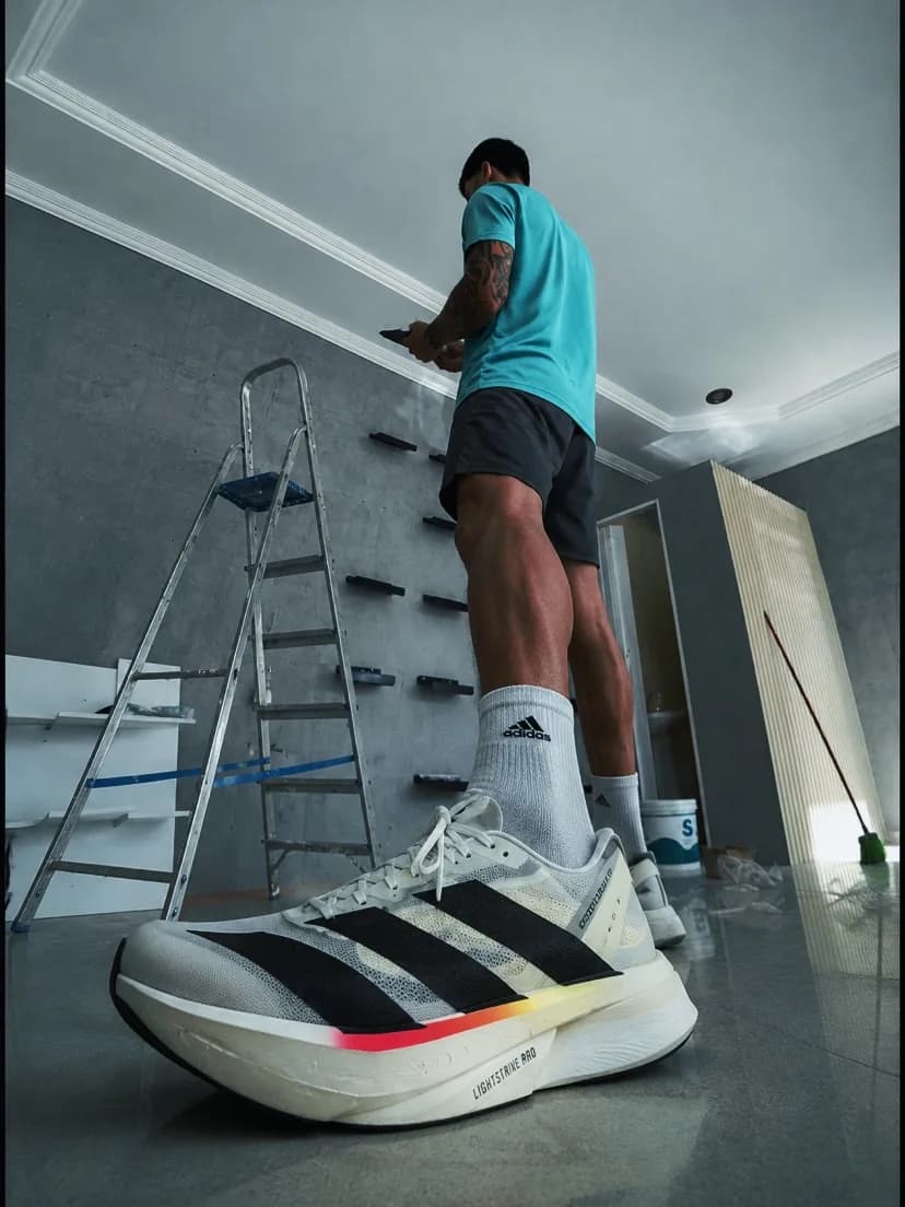 Na loja em Natal, alguém montando a parede de prateleiras, com um Adizero branco em primeiro plano